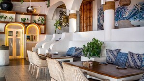 Un espacio lounge moderno con muebles de mimbre, una mesa de madera y un área de descanso con cojines estampados.