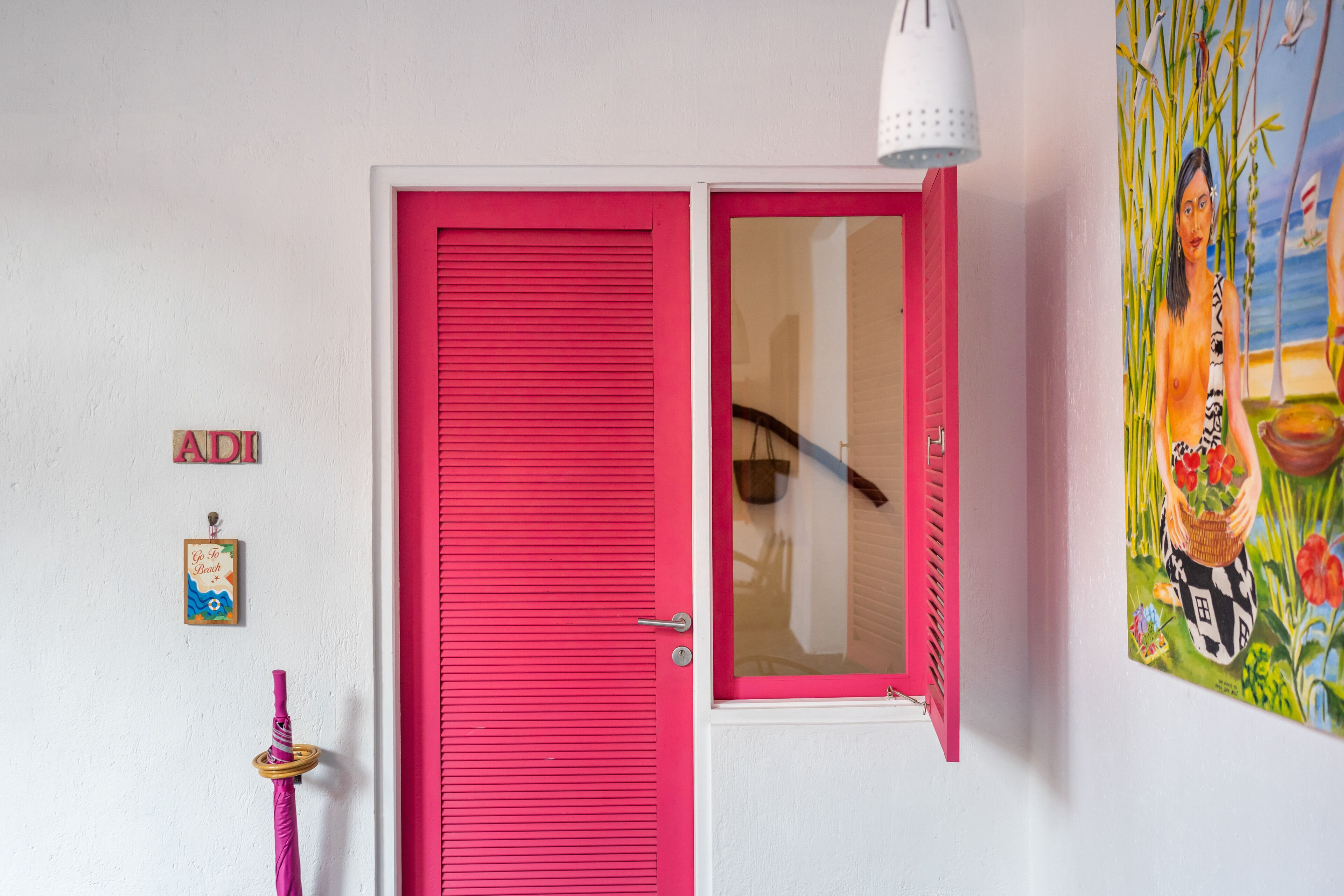 A bright pink door with a glass panel, a white wall with a painting, and a small sign with the letters "ADI".