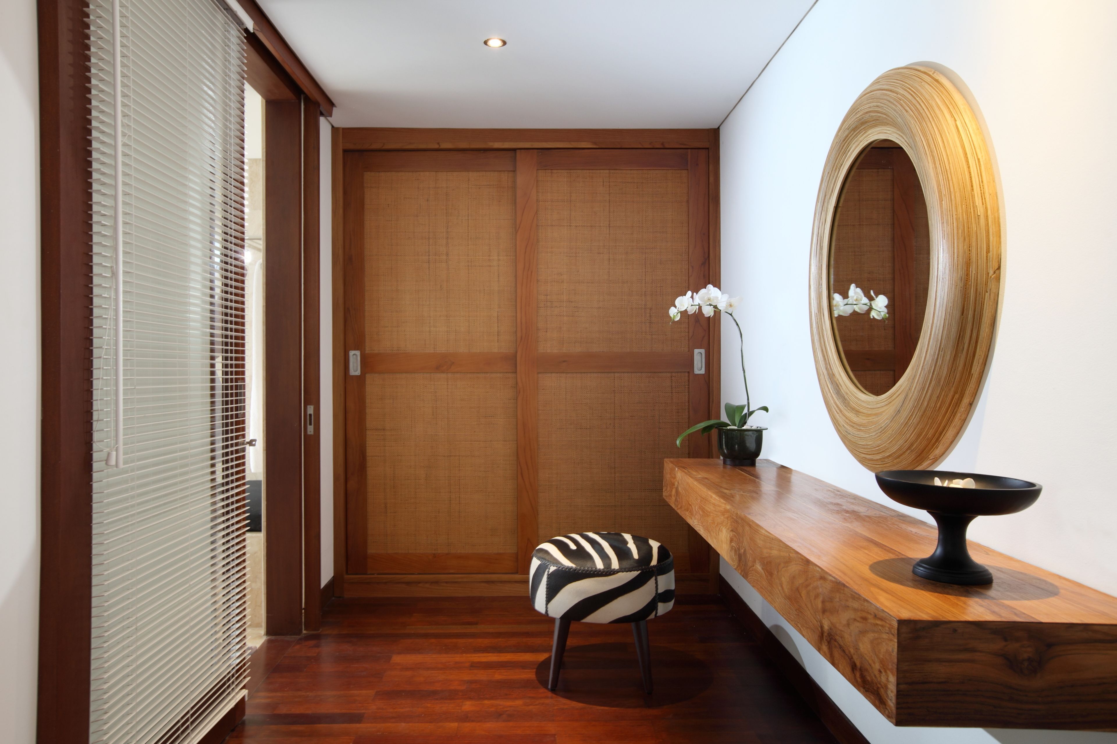 A modern hallway with a wooden floor, a sliding door, a bench, a wooden console table, and a large mirror.