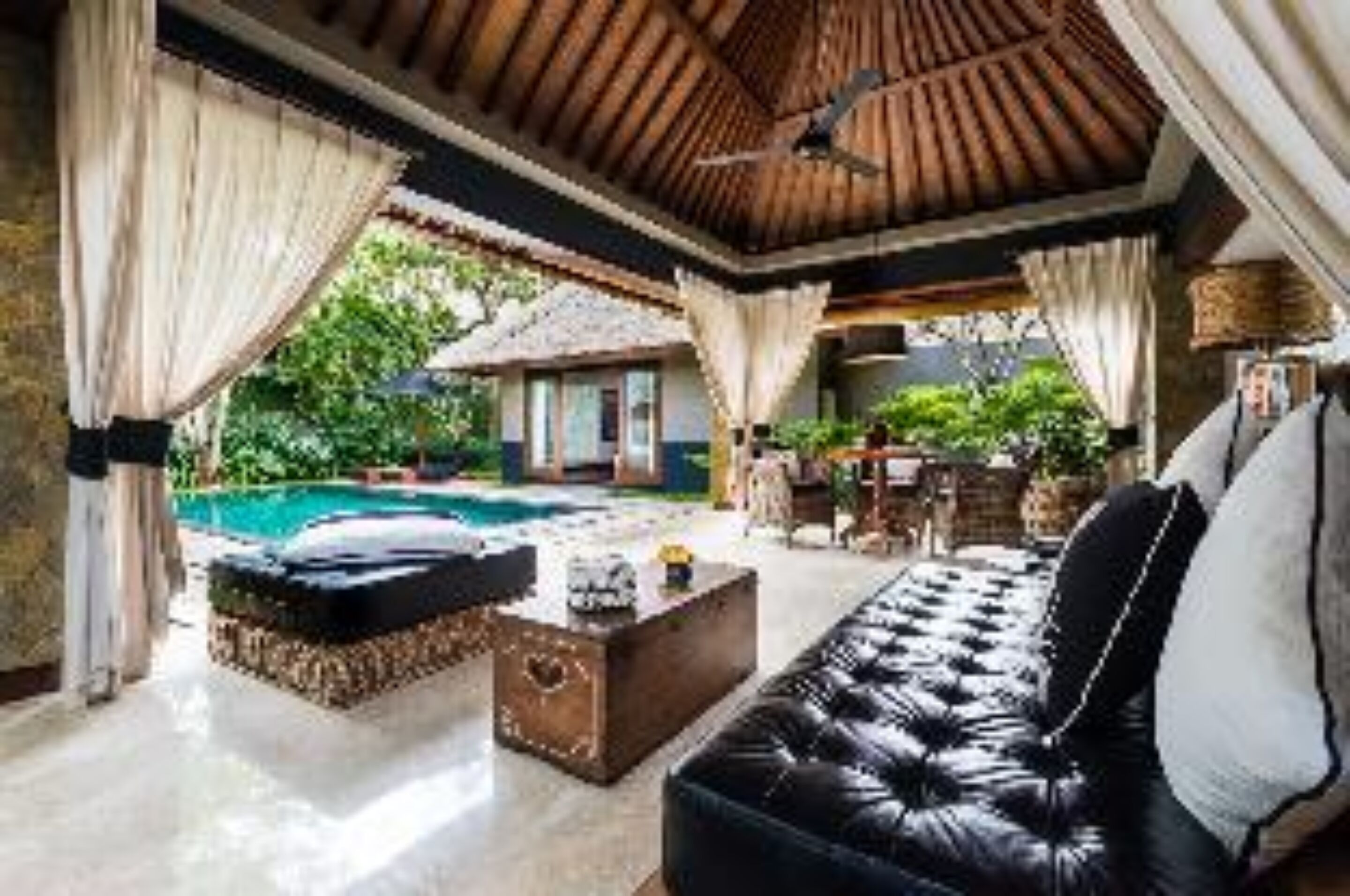 An indoor pool area with a black leather sofa, a wooden coffee table, and a thatched-roof structure in the background.