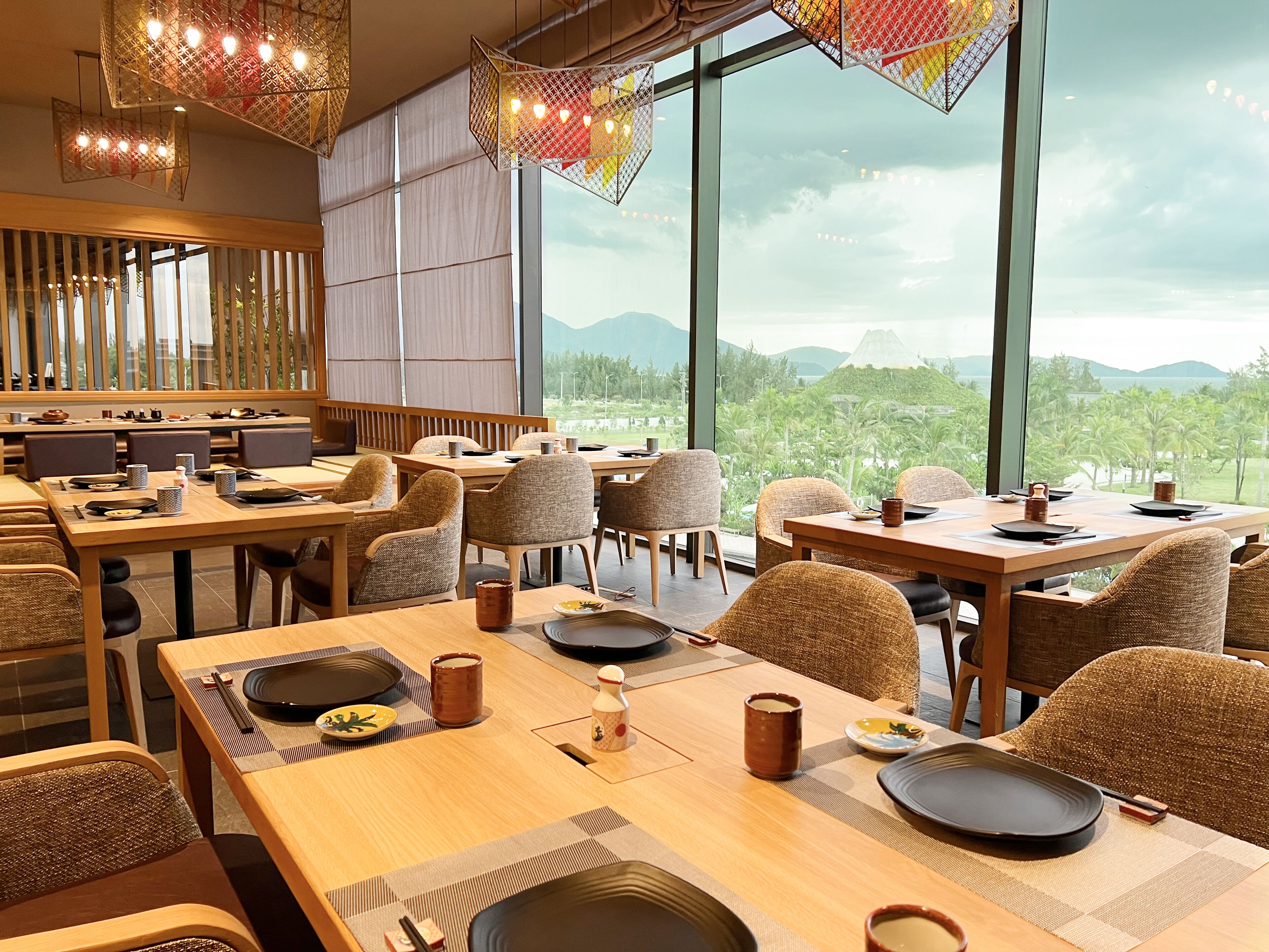 Un restaurante con mesas y sillas de madera, amplias ventanas que ofrecen vistas a la vegetación y montañas.