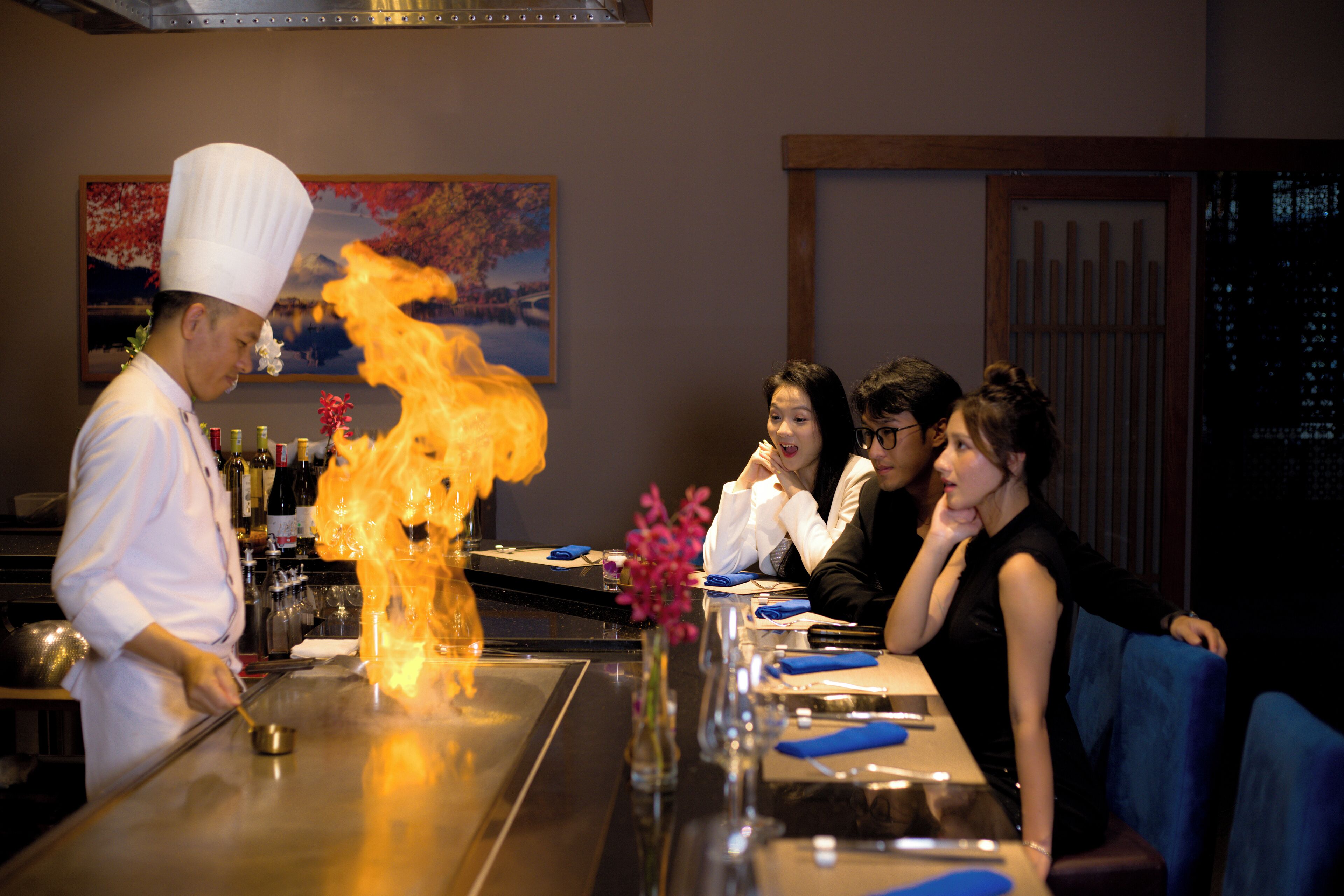 Ein Koch, der am Tisch in einem Restaurant eine Feuershow für Gäste aufführt.