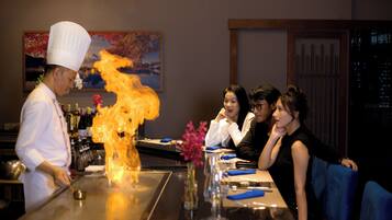 Ein Koch, der am Tisch in einem Restaurant eine Feuershow für Gäste aufführt.