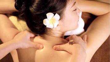 A person receiving a back massage in a room with a bed and a pillow.