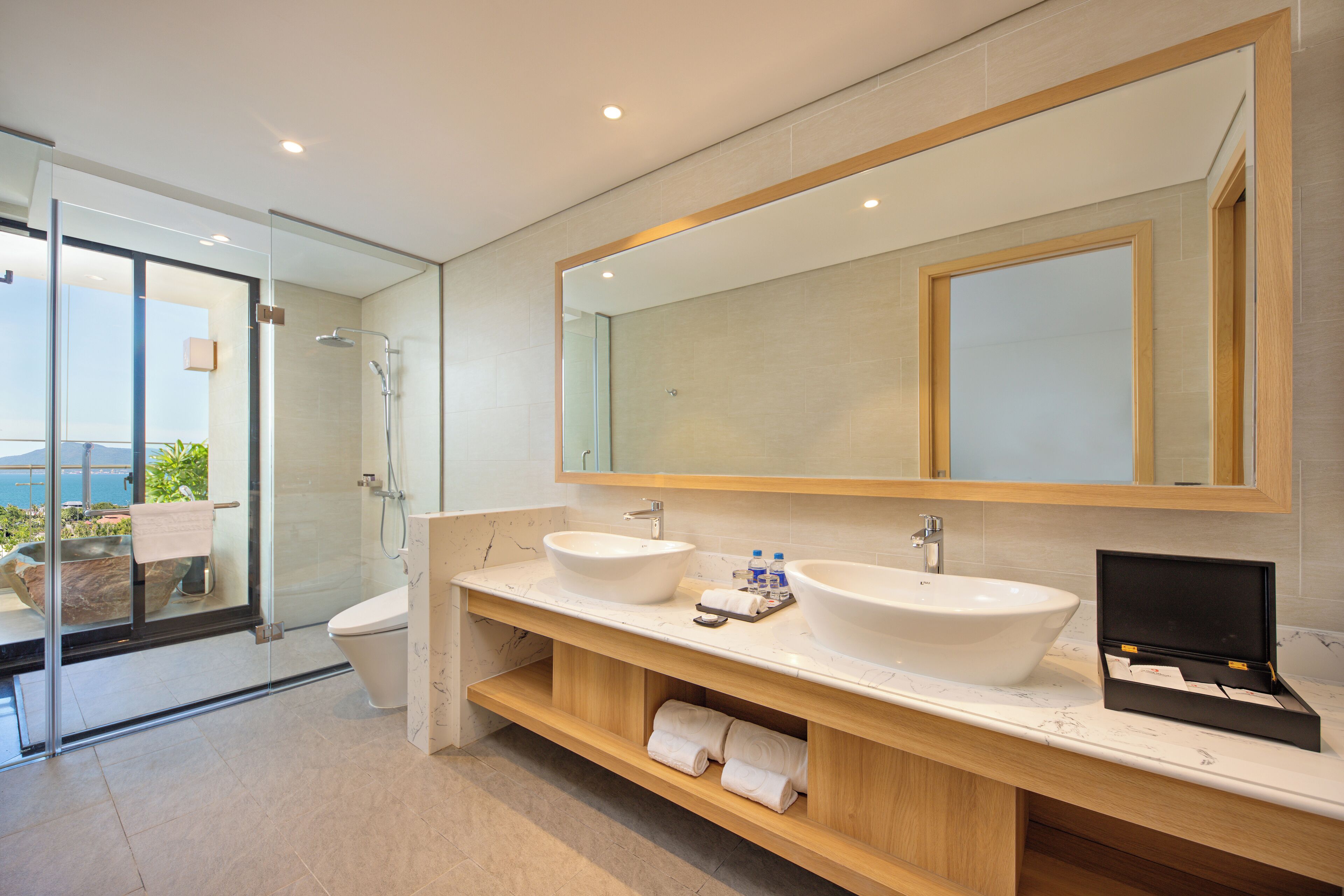 A modern bathroom with a glass shower enclosure, two sinks, a large mirror, and a wooden vanity.