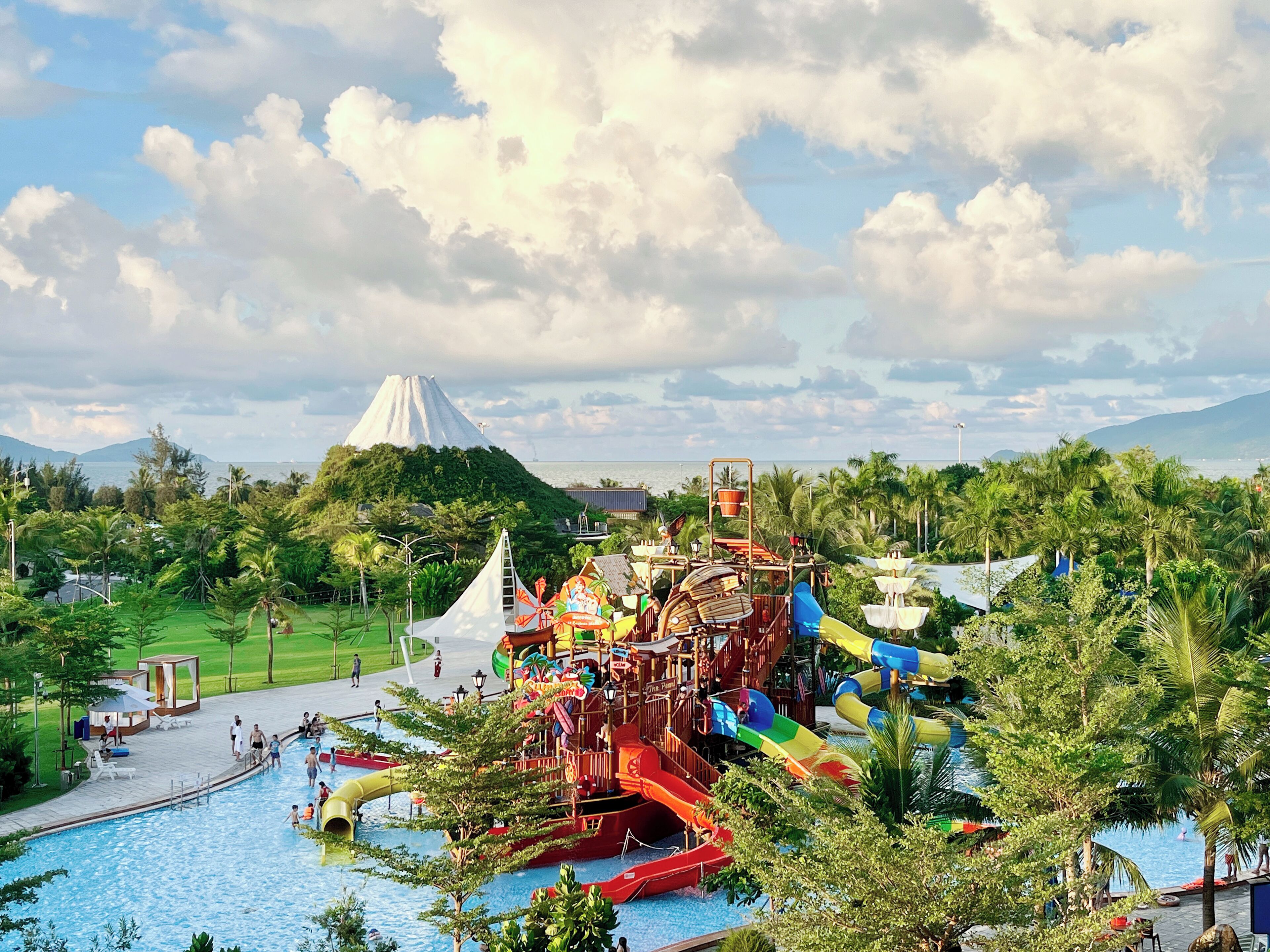 Parque acuático con toboganes y piscina, rodeado de vegetación y una montaña al fondo.