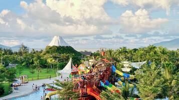 Parque acuático con toboganes y piscina, rodeado de vegetación y una montaña al fondo.