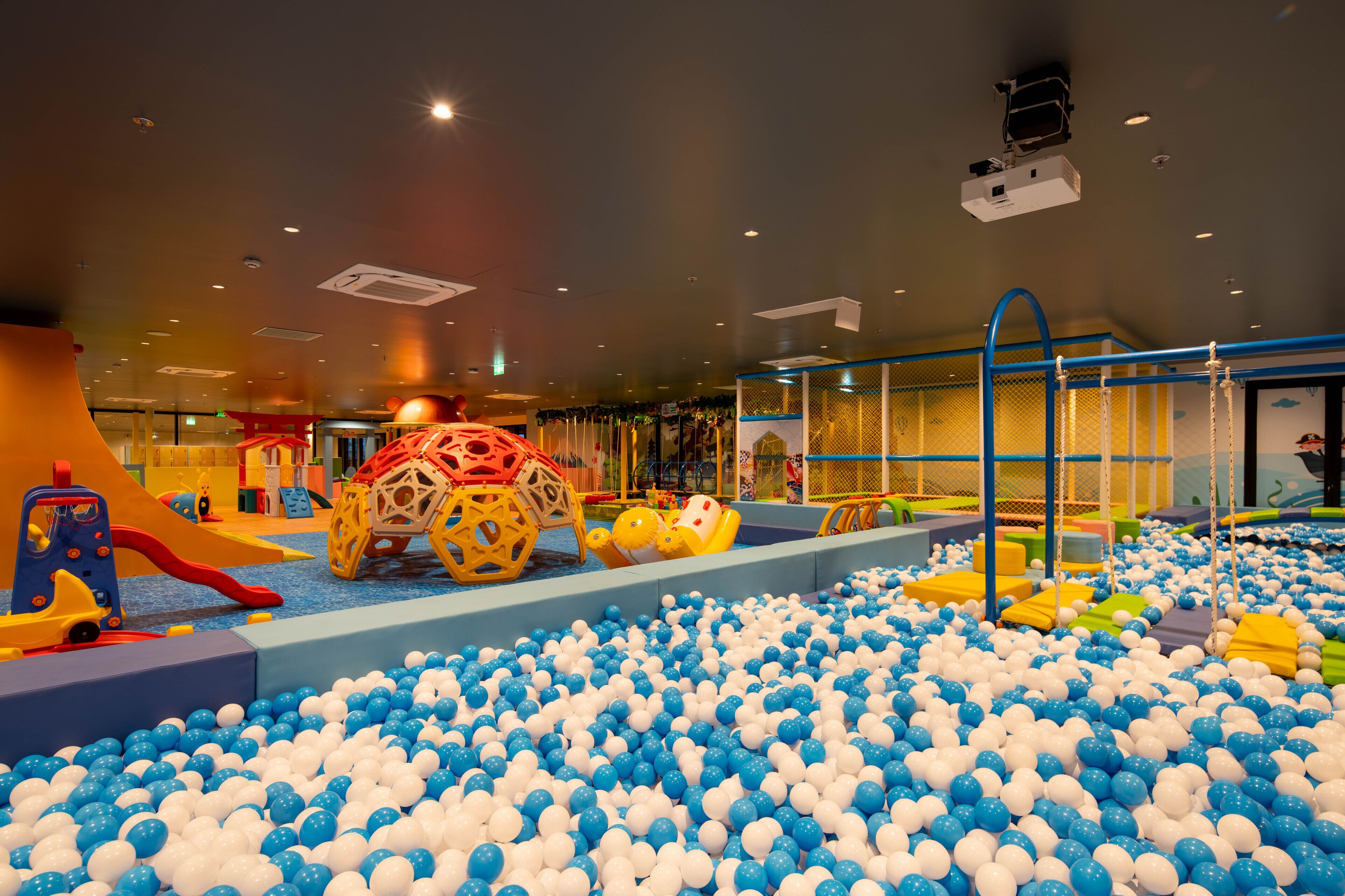 Zona de juegos infantiles con piscina de pelotas, toboganes y diversas estructuras recreativas.