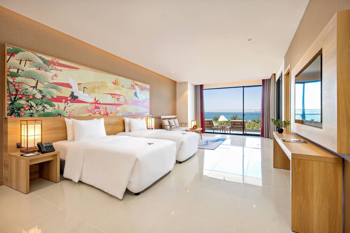 Een moderne hotelkamer met twee bedden, een groot schilderij, een bureau en uitzicht op zee.
