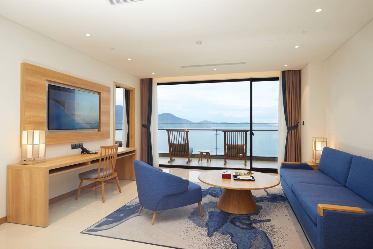 Een moderne hotelkamer met een groot raam, een flatscreen televisie, een bank, een bureau en een eethoek.