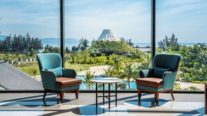 Una habitación con dos sillas y una mesa, amplias ventanas que ofrecen vistas a un volcán y una playa.