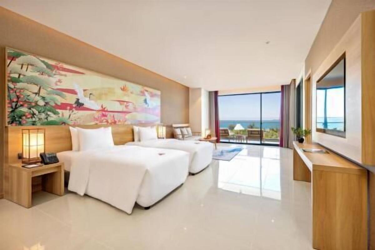 Een hotelkamer met een groot bed, een kleiner bed, een bureau en een groot raam met uitzicht op zee.