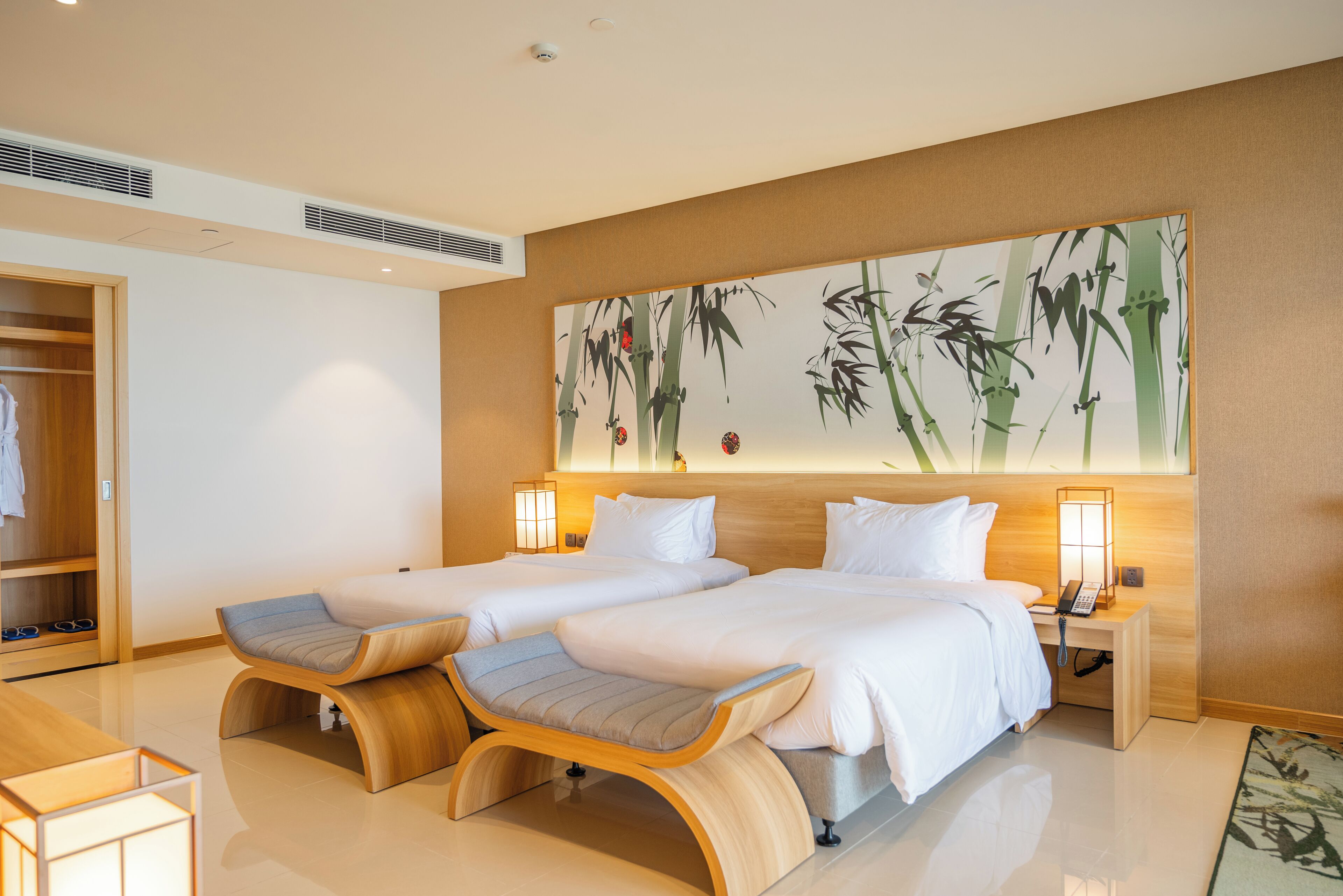 A hotel room with two beds, a wooden bench, a wardrobe, and a large wall painting.