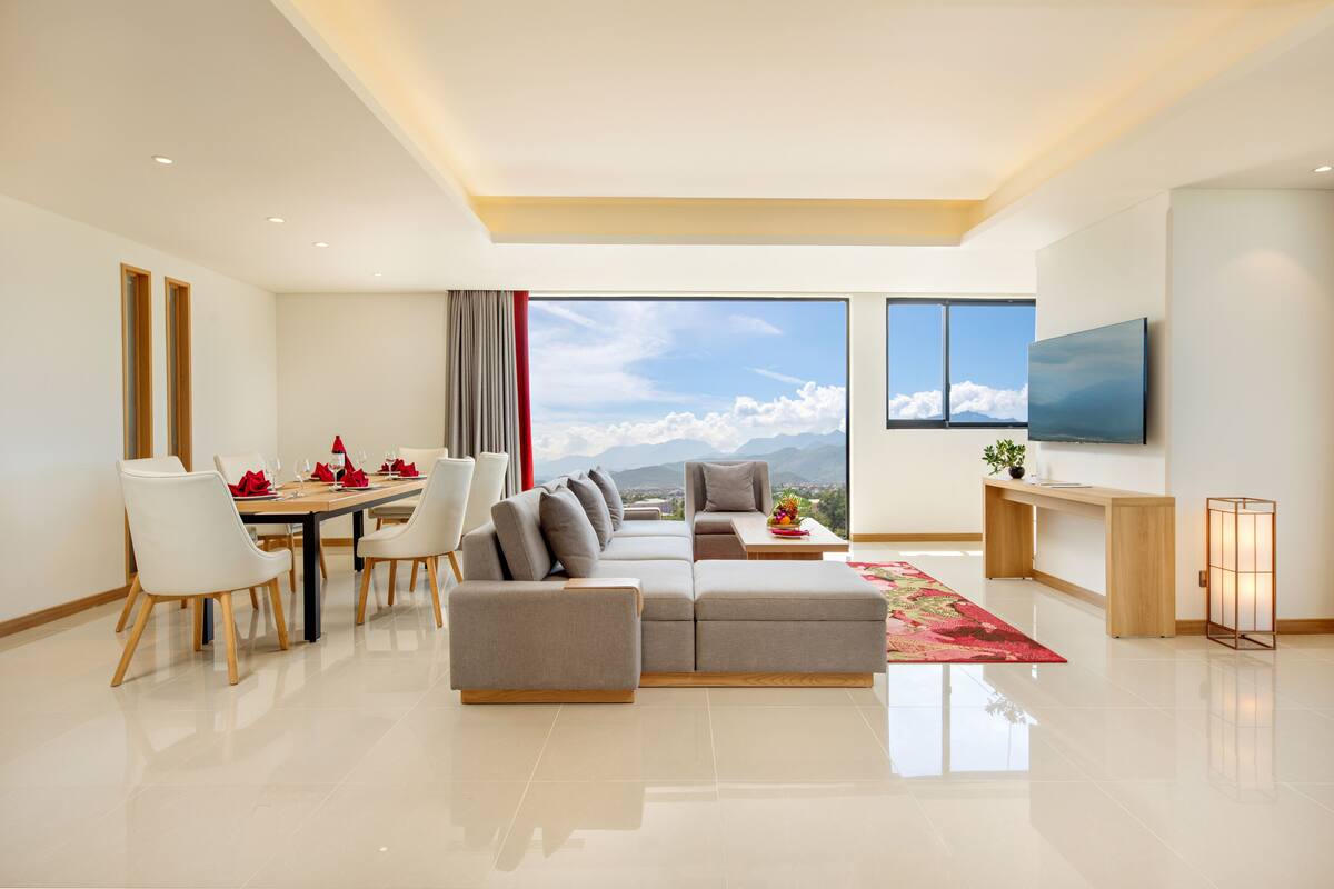 Een moderne woonkamer met een grote hoekbank, een eethoek met witte stoelen, een flatscreen-tv en uitzicht op de bergen.