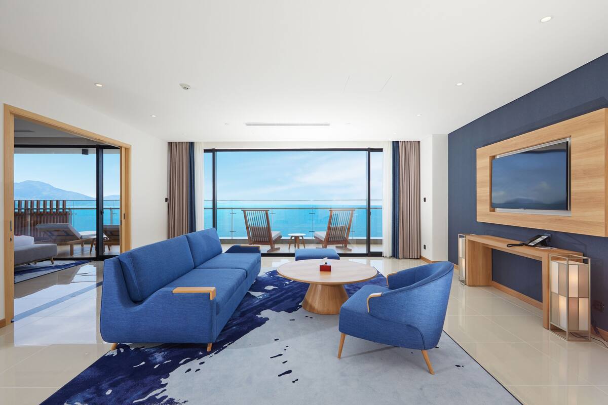 Een moderne woonkamer met een blauwe bank, een ronde salontafel en een aan de muur bevestigde televisie.
