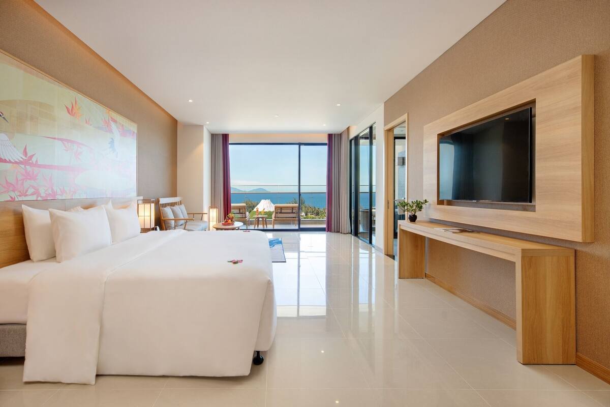 Een moderne hotelkamer met een groot bed, een flatscreen televisie, een balkon met uitzicht op zee en een schilderij aan de muur.