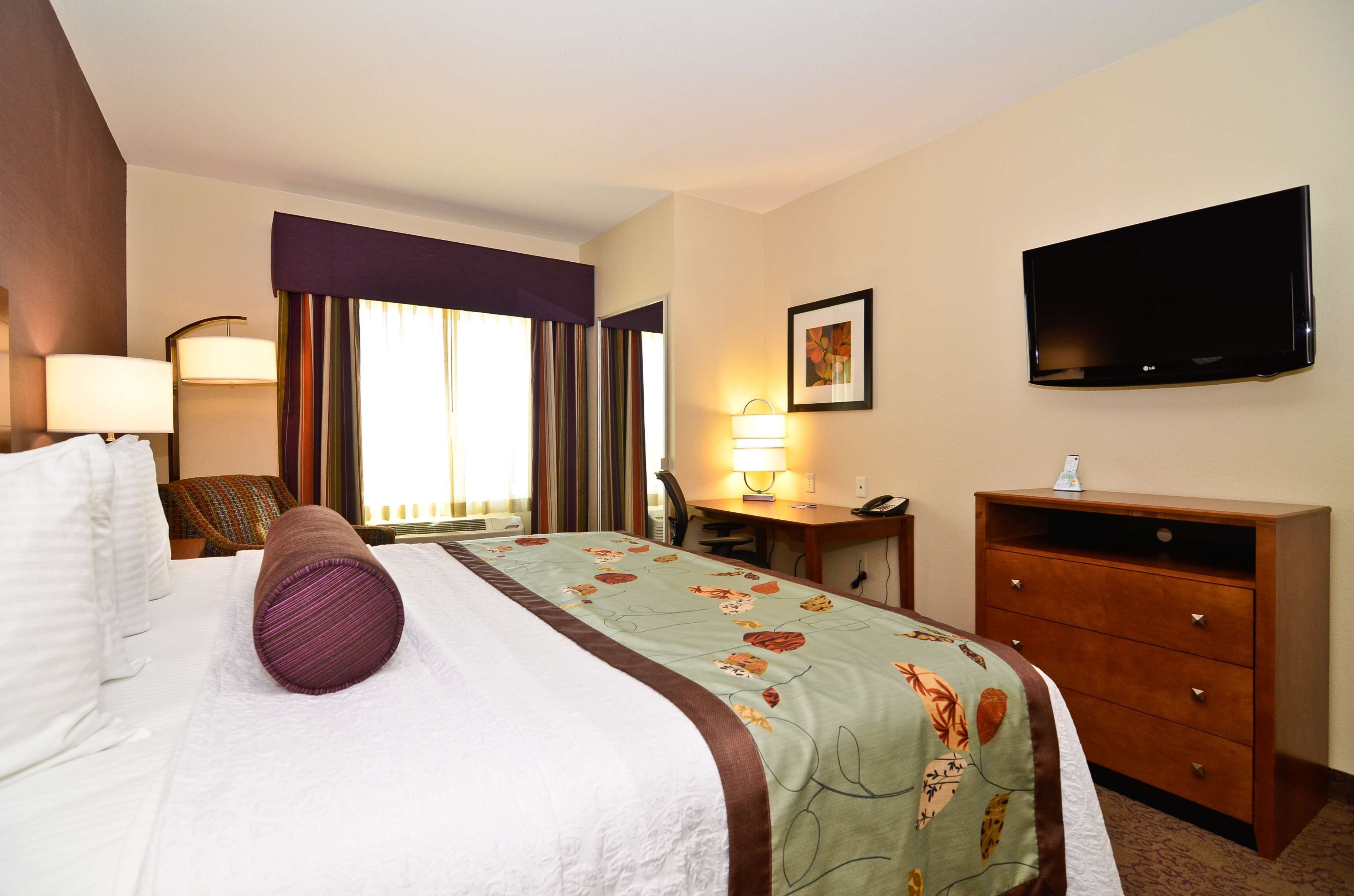 A hotel room with a bed, a desk, a chair, a television, and a dresser.