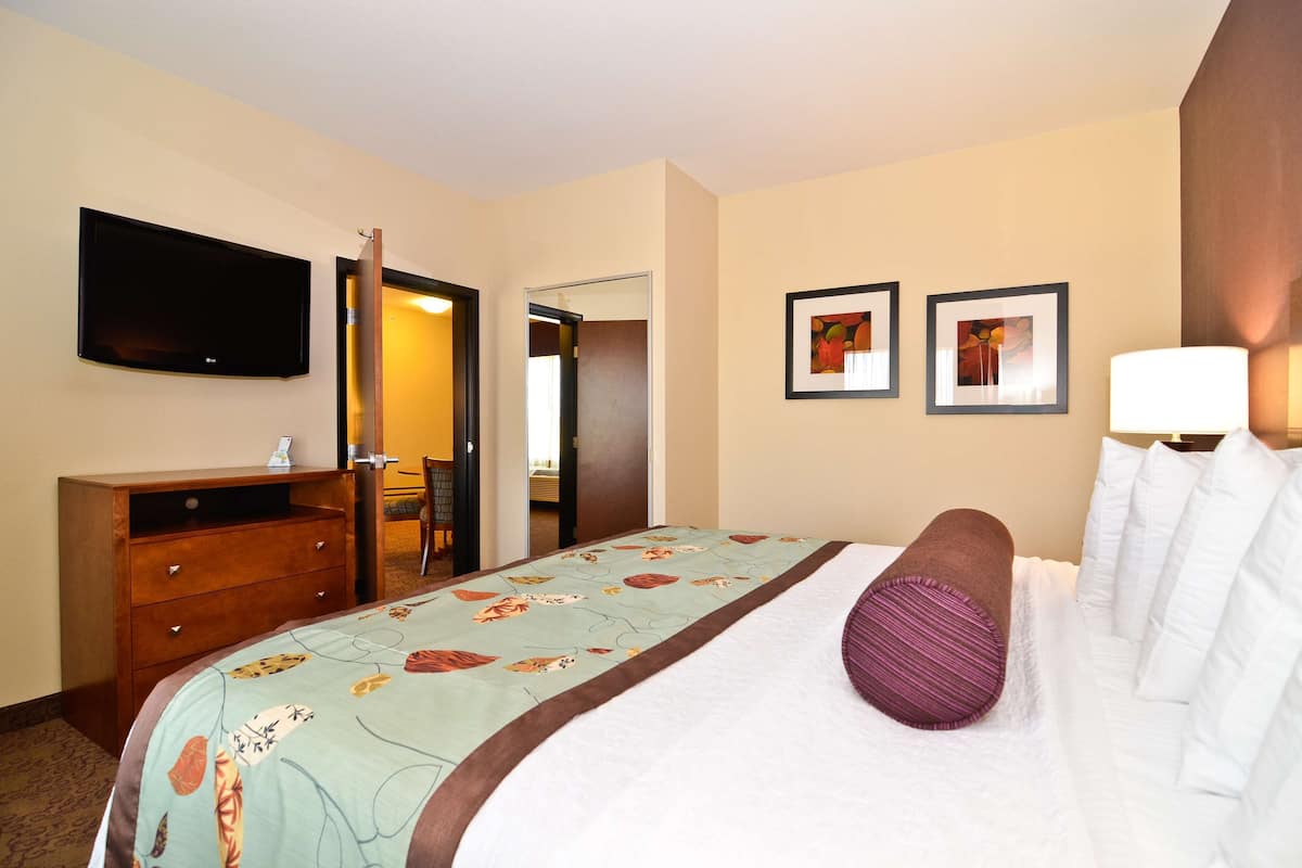 A hotel room with a bed, a TV, a desk, and two framed pictures on the wall.