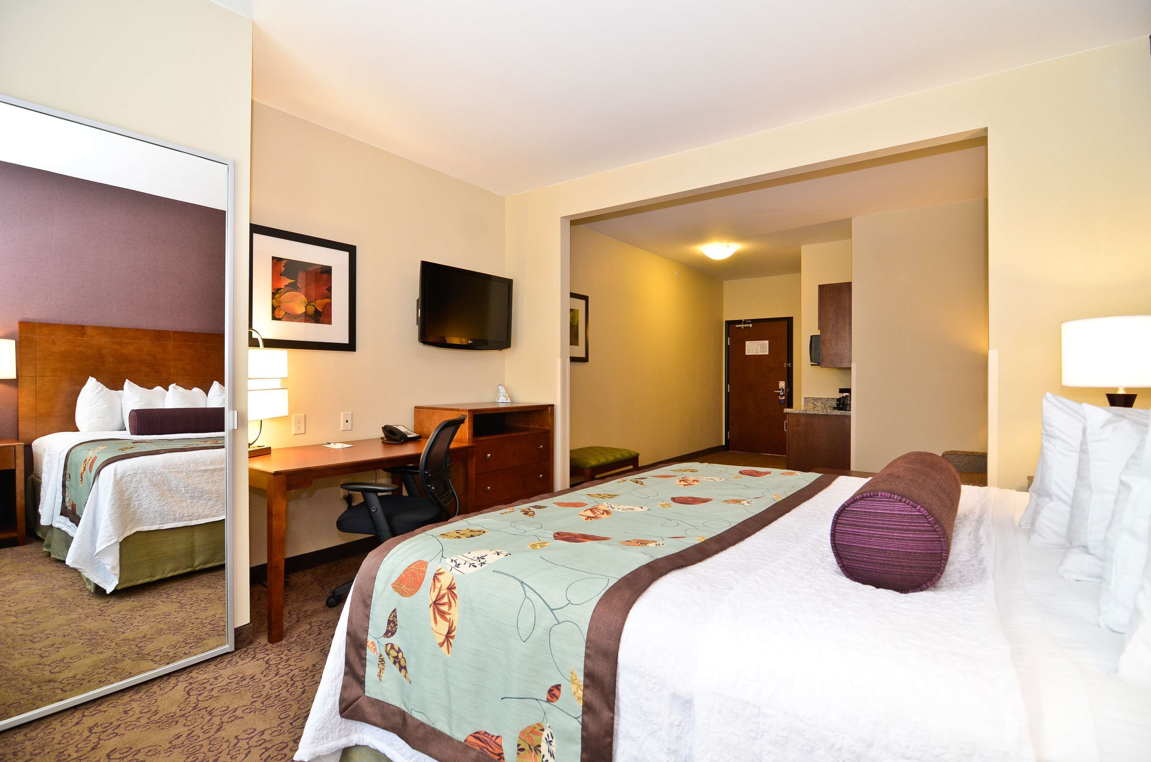 Une chambre d’hôtel équipée d’un lit, d’un bureau, d’une chaise, d’une télévision et d’un miroir.