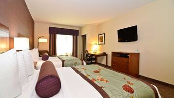 A hotel room with two beds, a desk, a chair, a TV, and a lamp.