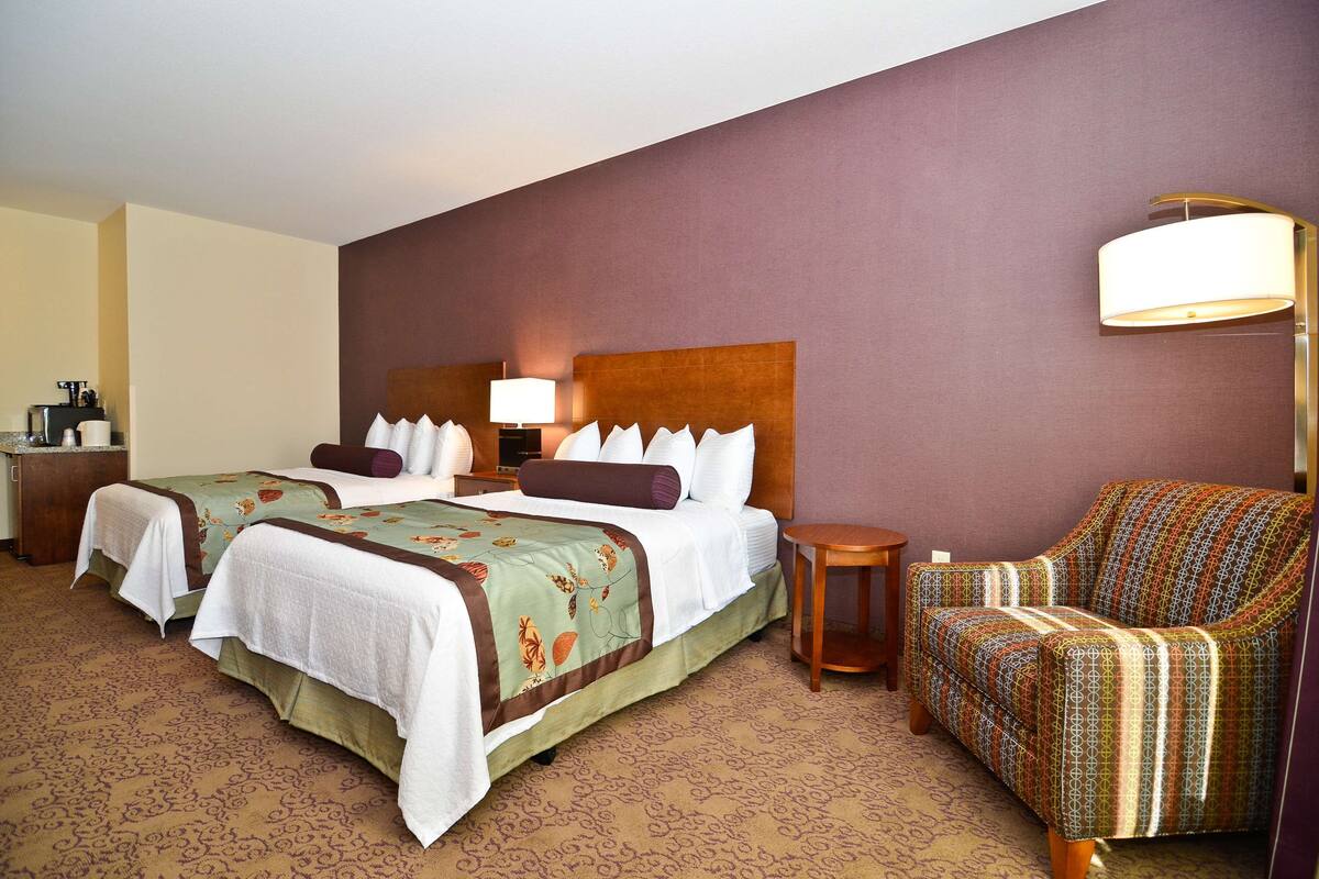 A hotel room with two beds, a sofa, a nightstand, and a lamp.