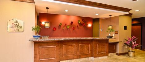 Un área de recepción con un mostrador de madera, un letrero que dice "Best Western Plus" y una pared con platos decorativos.
