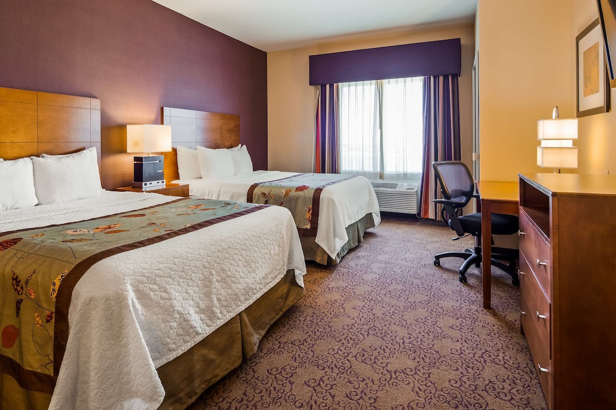 A hotel room with two beds, a desk, a chair, and a dresser.