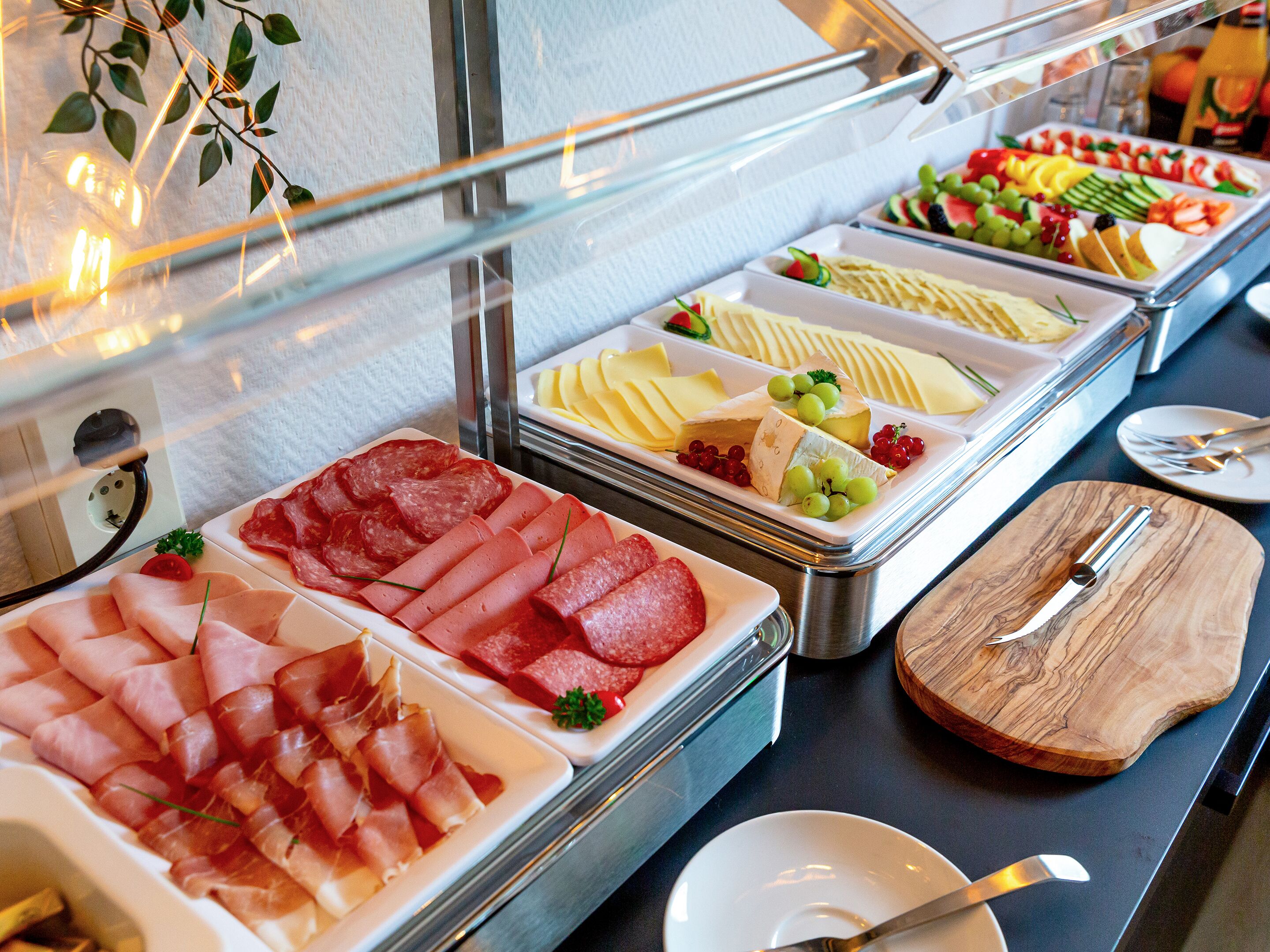 A buffet with various food options including meats, cheeses, and fruits.