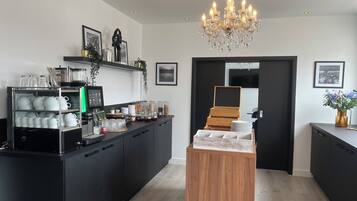 Une cuisine moderne dotée d’un coin café, de meubles noirs et d’une étagère en bois.