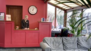 A reception area with a receptionist, a clock, a sofa, and a potted plant. - Best Western The Crianlarich Hotel (Crianlarich)