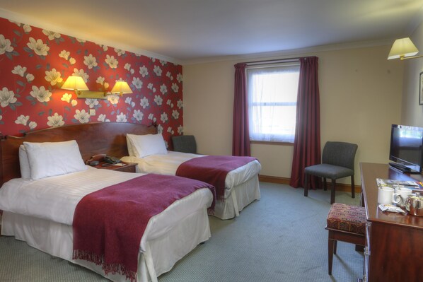 Une chambre d’hôtel avec deux lits, un bureau avec une télévision, une chaise et une fenêtre avec des rideaux.