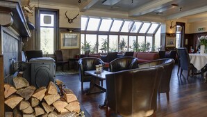 A cozy lounge with leather chairs, a fireplace, and a large window with a view of trees. - Best Western The Crianlarich Hotel (Crianlarich)