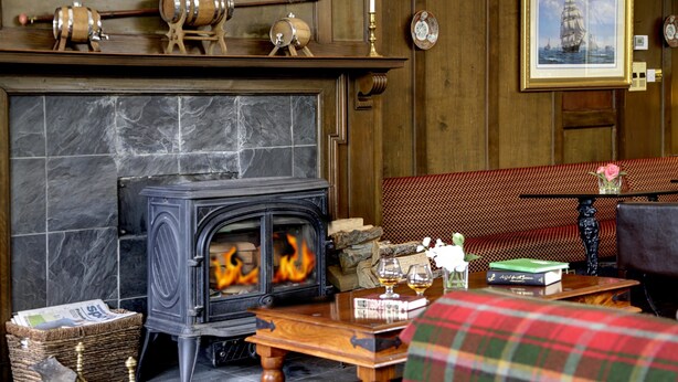 A cozy room with a stone fireplace, a wooden bench, and a table with a book and glasses. - Best Western The Crianlarich Hotel (Crianlarich)