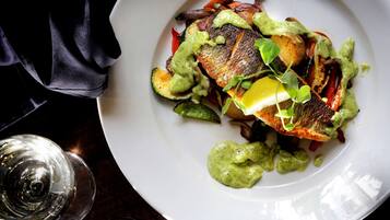 Un plato de comida con una porción de pescado, verduras y una cucharada de salsa verde.