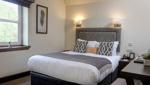 A neatly arranged bedroom with a large bed, bedside lamps, a small table with a plant, and a window with a view of greenery. - Best Western The Crianlarich Hotel (Crianlarich)