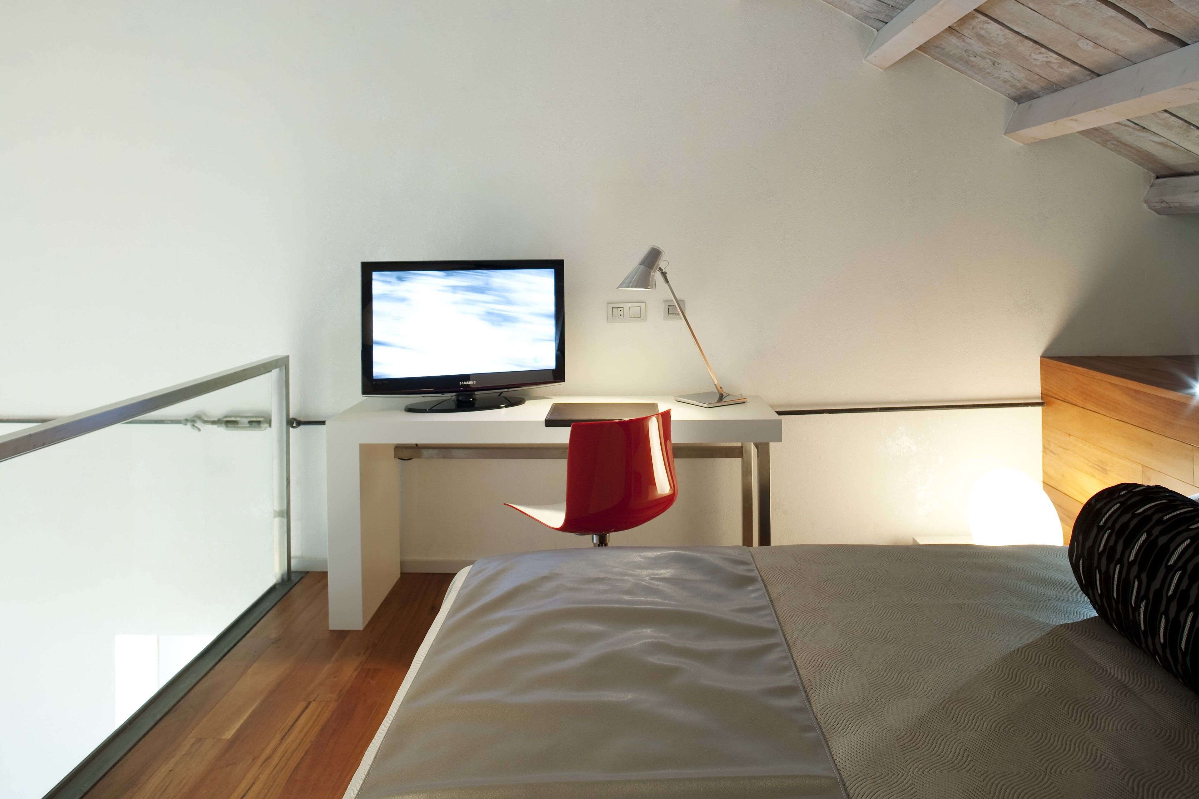 A bedroom with a bed, a desk with a computer monitor, and a red chair.
