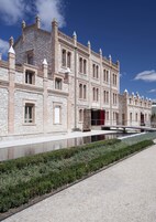 Un edificio histórico con fachada de piedra, amplias ventanas y una fuente reflectante en primer plano.