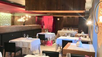 A restaurant with multiple tables set for dining, featuring white tablecloths and wine glasses.