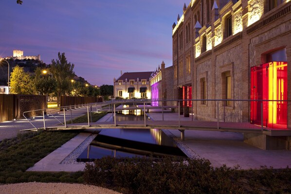 Un edificio histórico con un foso y un puente, iluminado con luz ambiental.