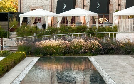 A pool area with a stone building in the background, outdoor seating with umbrellas, and a well-maintained garden.