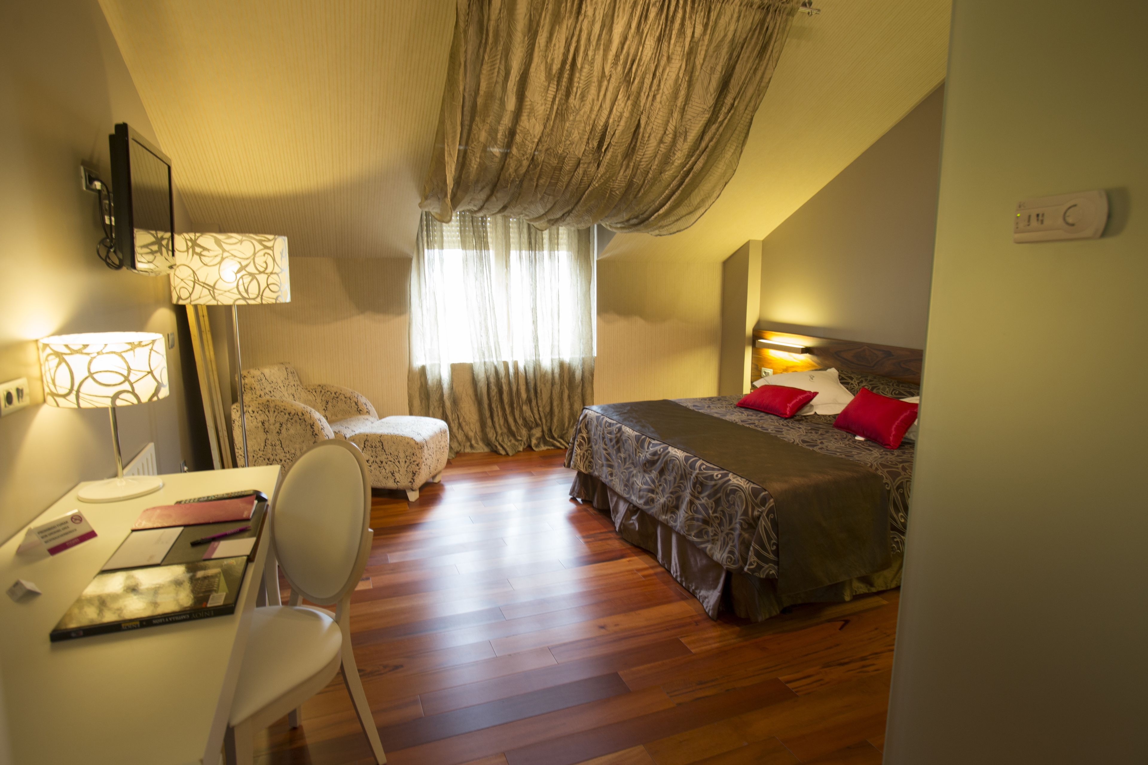 A bedroom with a bed, a desk, a chair, and a window with curtains.
