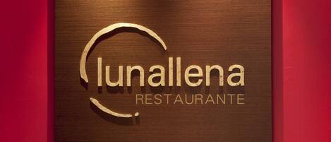 Ein Schild mit dem Schriftzug "lunallena RESTAURANTE" auf einer Holzplatte vor einer roten Wand.