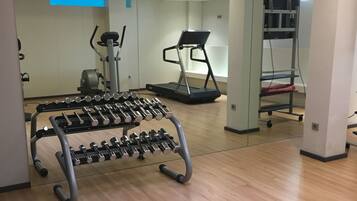 A gym with a mirrored wall, a treadmill, and a rack of dumbbells.