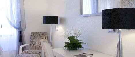 Una habitación moderna y luminosa con un escritorio blanco, dos sillas, una lámpara negra y un espejo.
