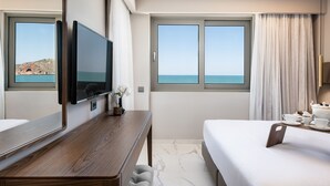 A hotel room with a large bed, a TV, a desk, and a view of the sea.