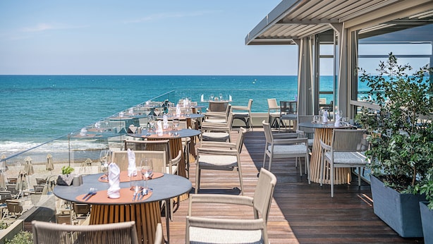 An outdoor dining area with tables and chairs overlooking the sea.