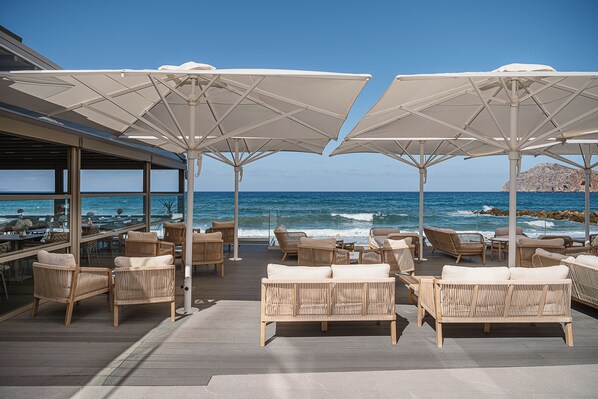 A beachside patio with wicker furniture and large umbrellas, overlooking the ocean. - Porto Platanias Beach - Luxury Selection (Chania)
