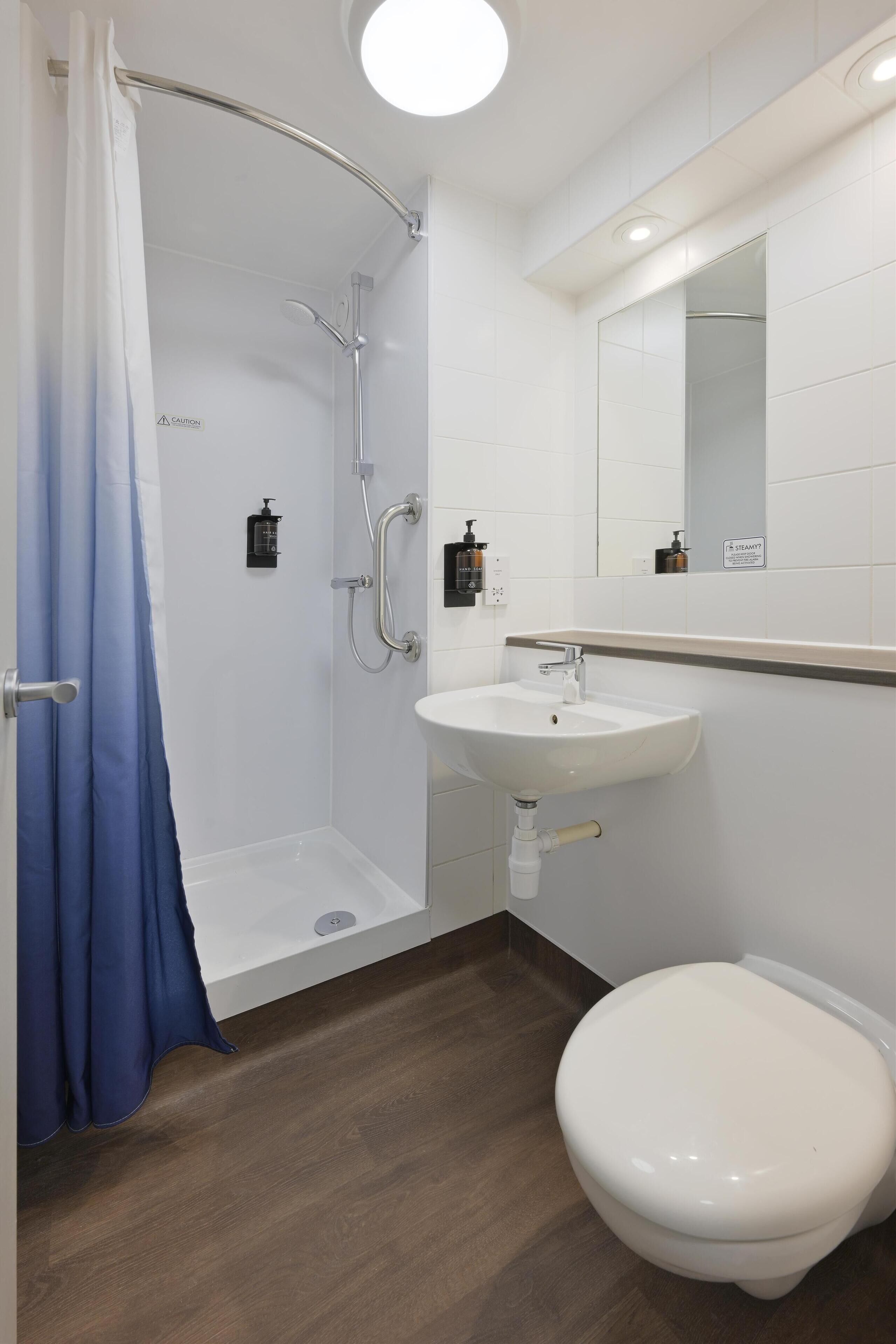 A bathroom with a shower, sink, toilet, and a mirror.