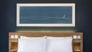Una cama bien hecha con ropa de cama blanca, un cabecero de madera y una obra enmarcada encima.