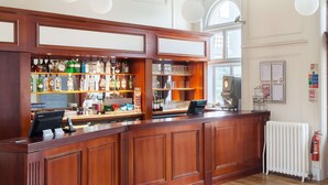 Un espace bar avec des panneaux de bois, des étagères remplies de bouteilles d’alcool, une caisse enregistreuse et une machine à café.